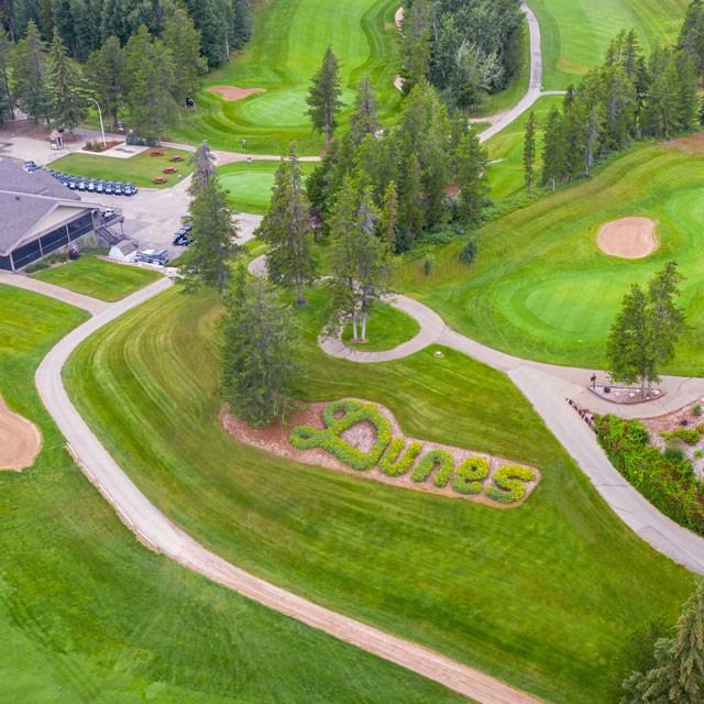 Aerial view of The Dunes Golf & Winter Club with winding cart paths, greens, trees, and clubhouse.