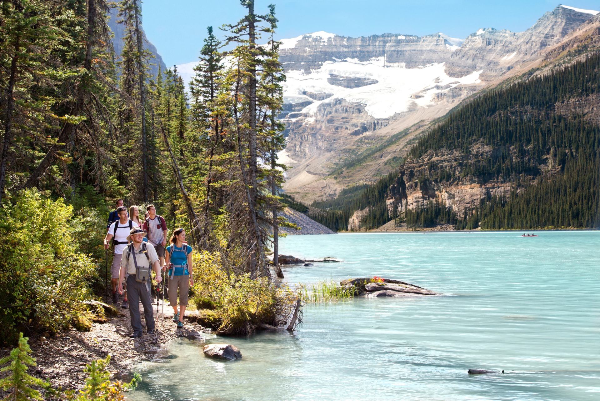 Hikers walk beside turquoise lake with mountains at Lake Louise.