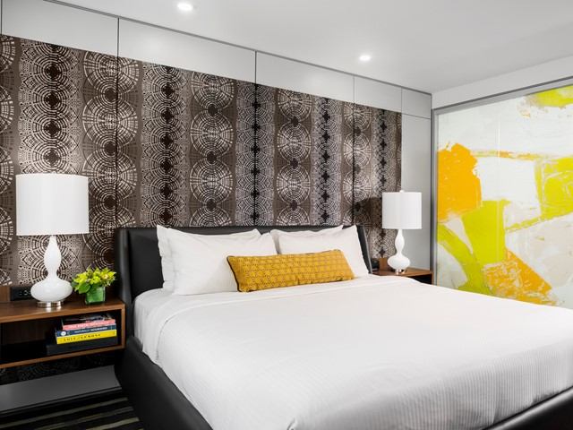 Stylish hotel room with white linens, yellow pillow, and colorful abstract wall art.