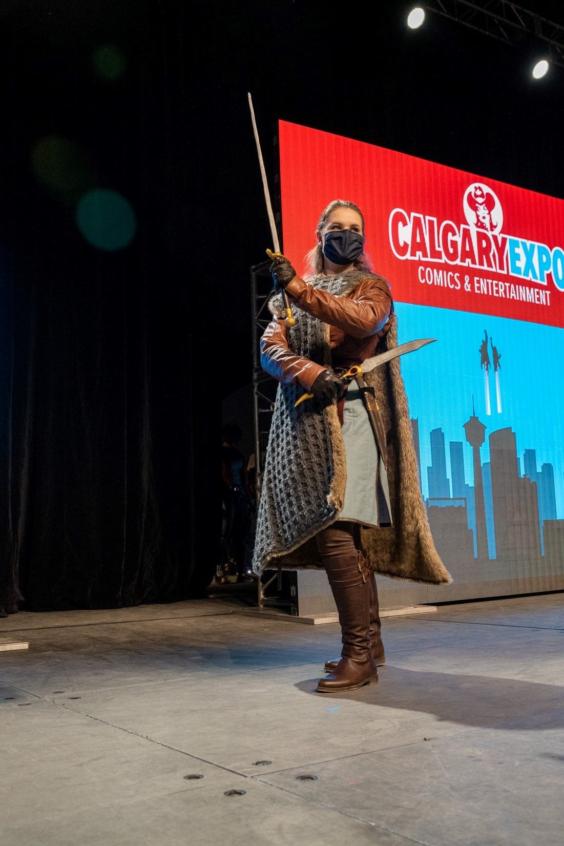 Cosplayer in medieval armor poses with sword on stage at Calgary Comic and Entertainment Expo.