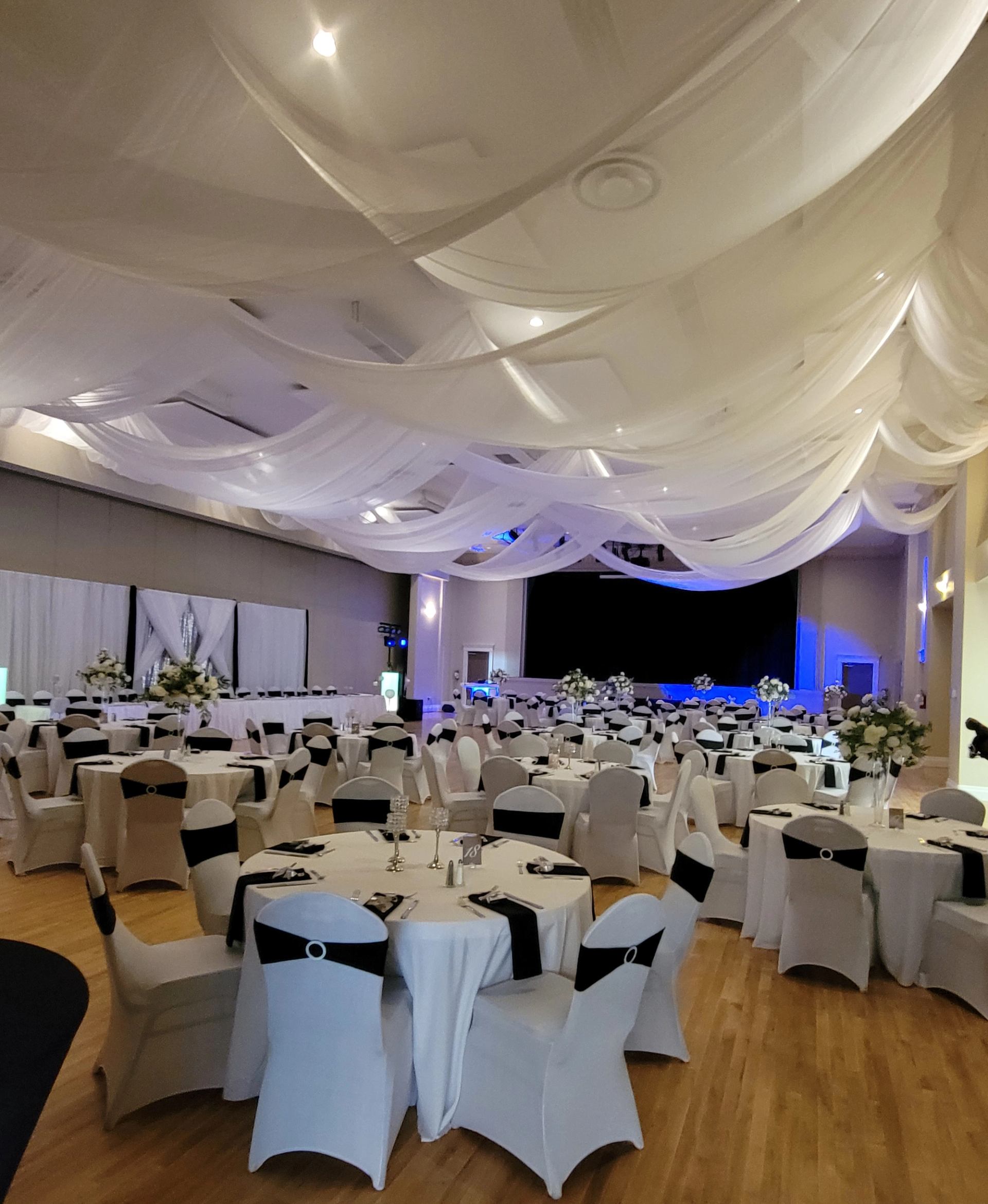Large event hall with round tables, white chair covers, and flowing ceiling drapes