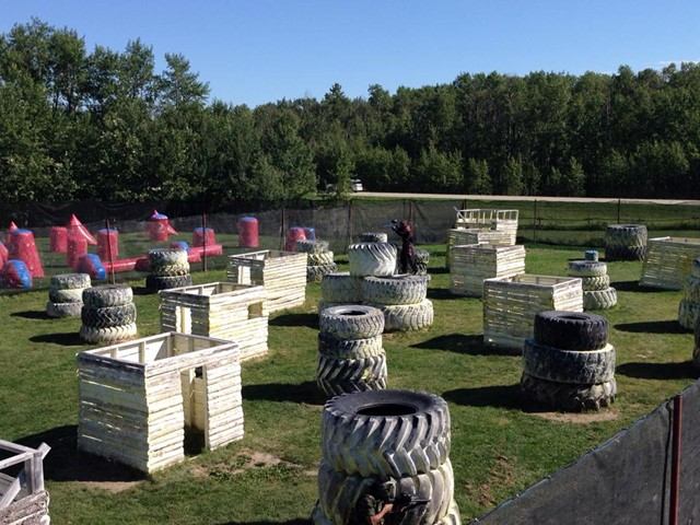 Paintball field with tires, hay bales, and barriers on a grassy outdoor range.