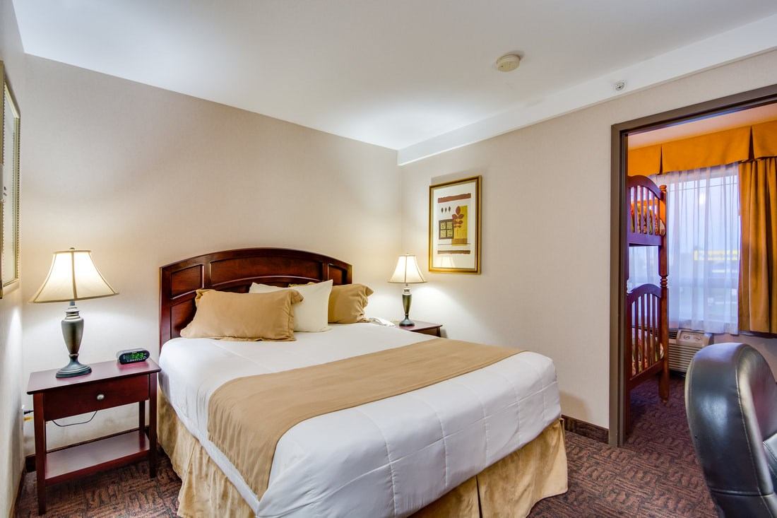 Cozy hotel suite with large bed, warm lighting, and adjoining bunk bed area.
