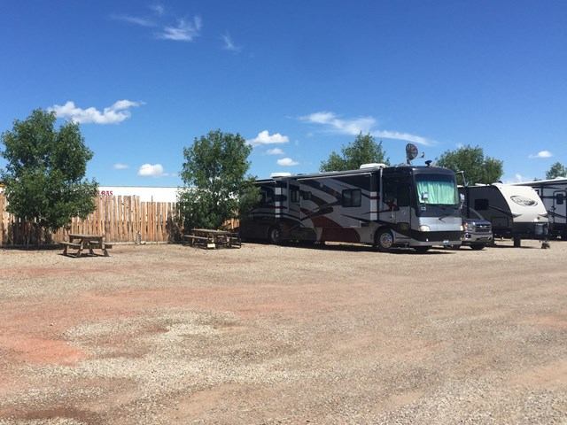 RVs parked on a gravel lot at Elbas Farms RV Park under a bright blue sky.