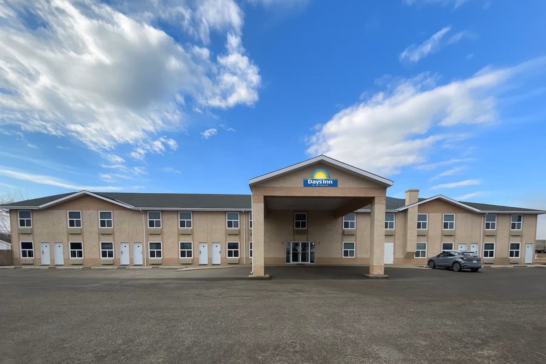 Exterior view of a two‑story Days Inn with a covered entrance, beige facade, and a paved parking area.