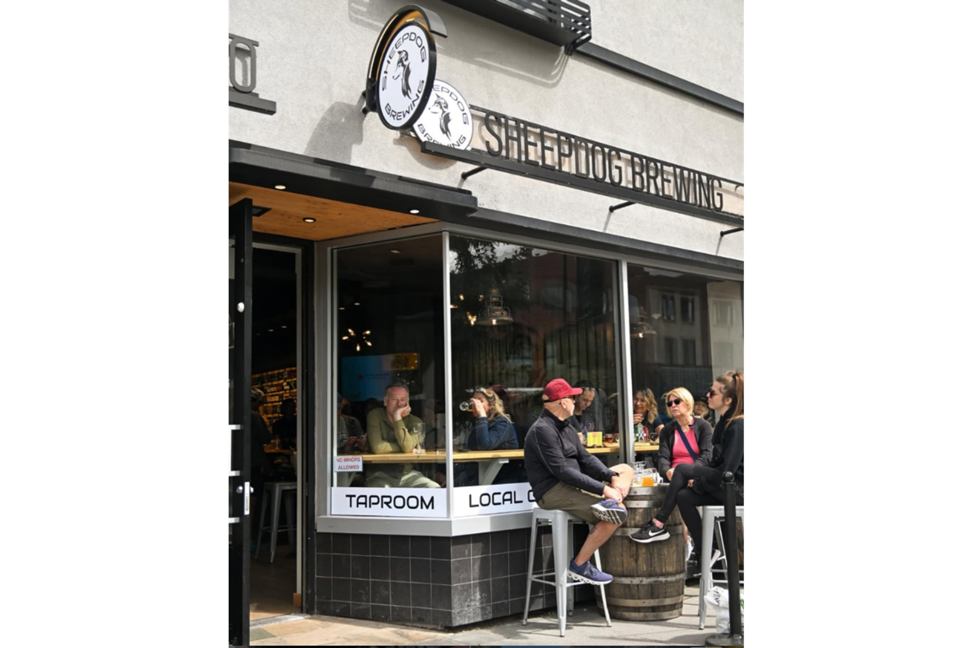 Patrons sit inside and outside Sheepdog Brewing taproom beneath storefront signage.