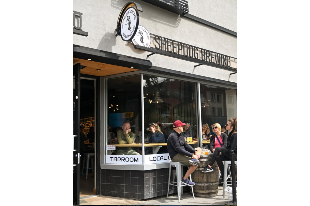 Patrons sit inside and outside Sheepdog Brewing taproom beneath storefront signage.