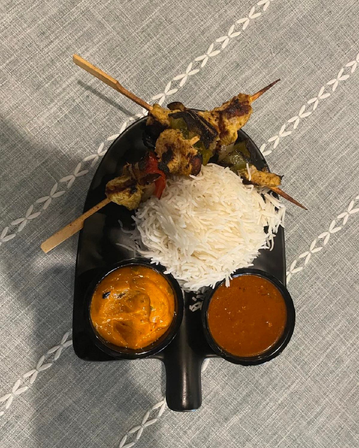 Grilled chicken skewers with rice and two dipping sauces on a shovel-shaped plate.