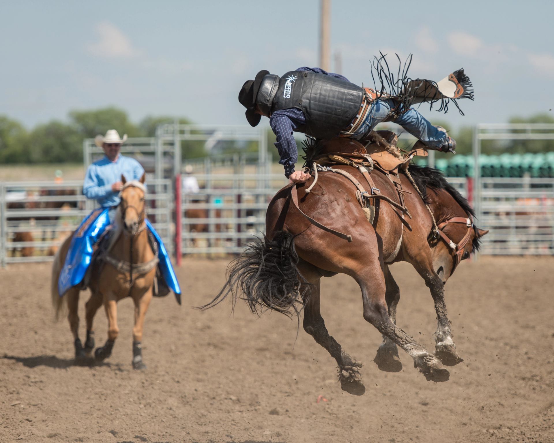 Rodeo rider bucking on a jumping horse while another rider watches in arena.