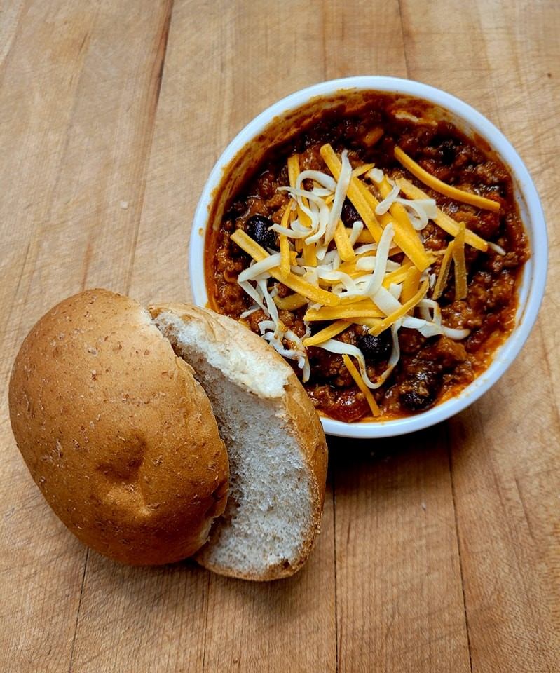 Bowl of chili topped with shredded cheese served with a fresh bun at Lakeview Bakery & Deli.