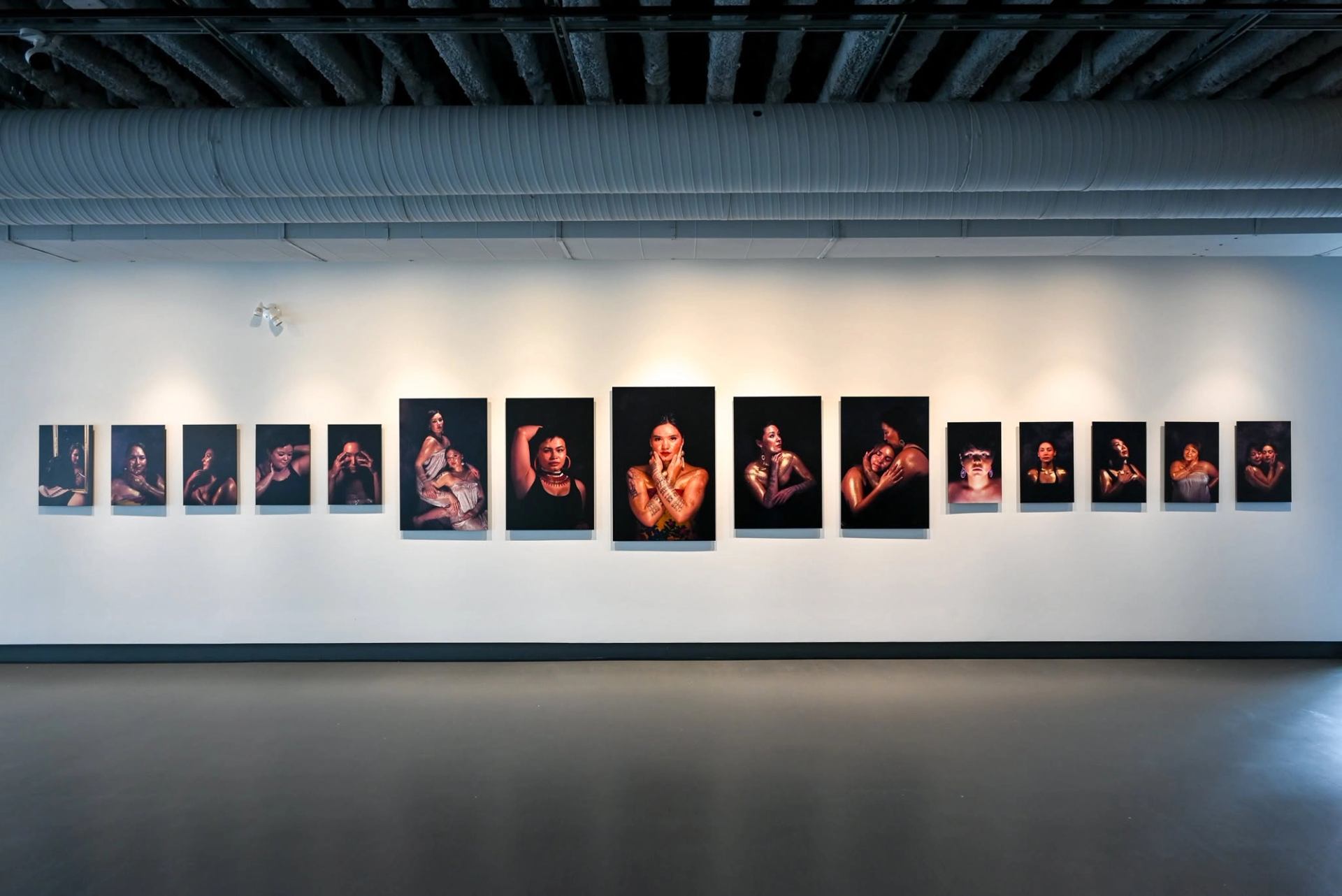 Gallery wall displaying framed portrait photographs of people against dark backgrounds under spotlights.