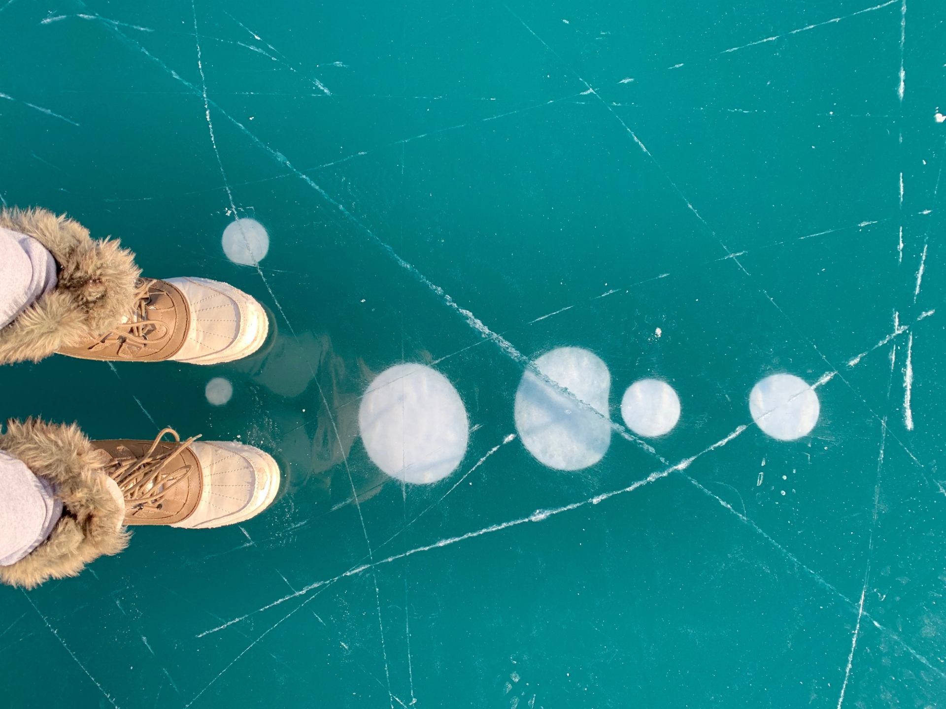 Close-up of boots standing on clear ice at Abraham Lake with visible methane bubbles underneath.