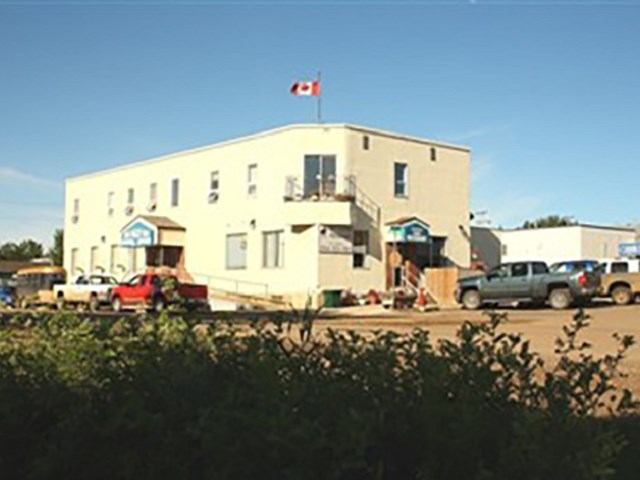 Two-storey beige commercial building with Canadian flag and parked pickup trucks in front.