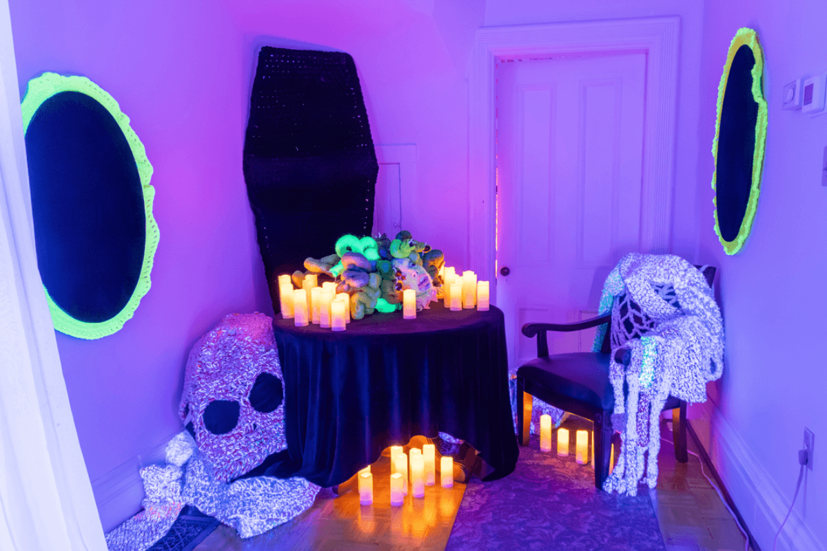 Neon-lit room with skull sculptures, coffin, candles and oval wall decorations.