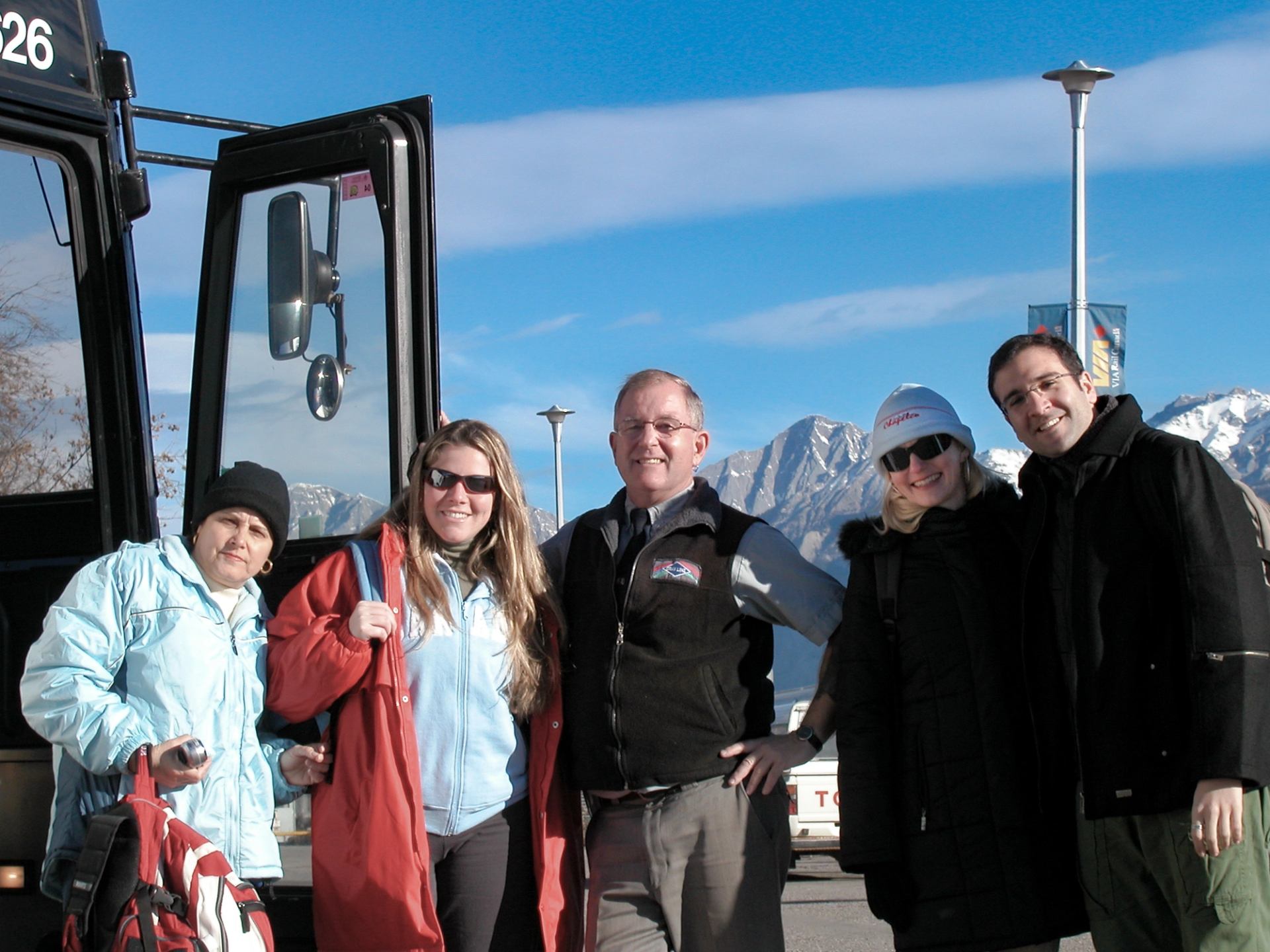 A group standing beside a tour bus with rugged mountains in the background.