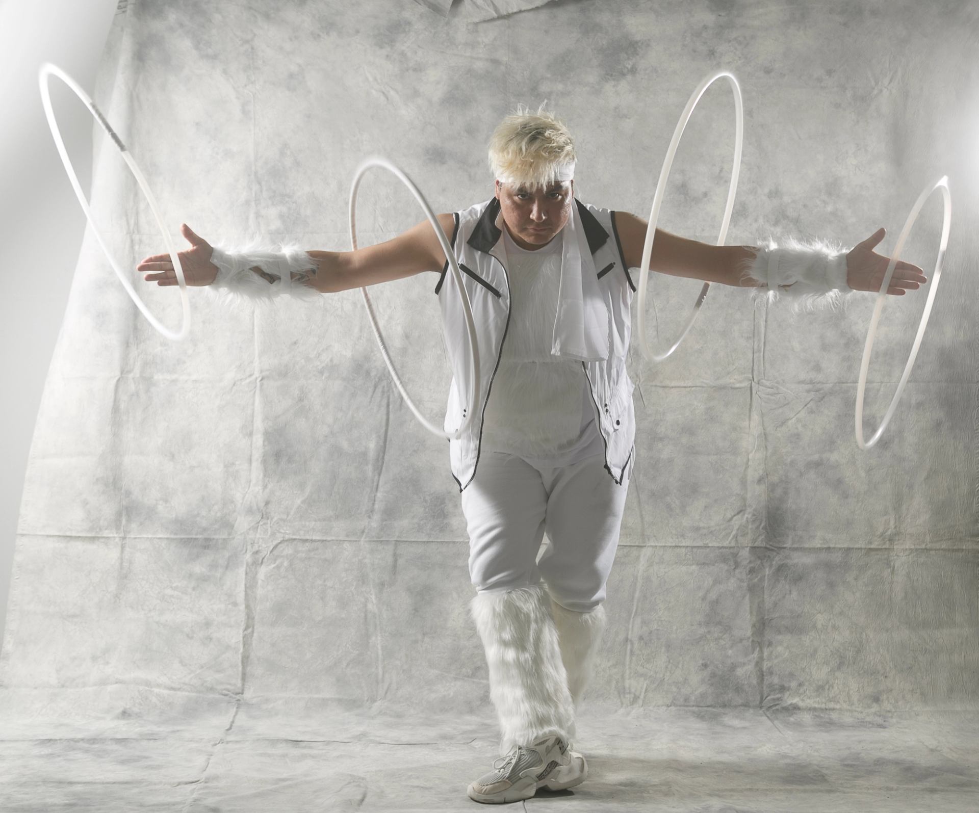 Performer in white costume spins glowing hoops in front of light grey backdrop.