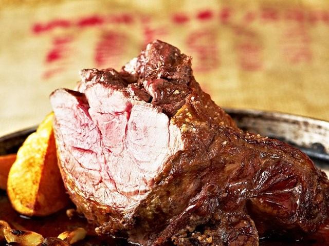 Roasted meat with charred edges on a platter, with bread pieces beside it.
