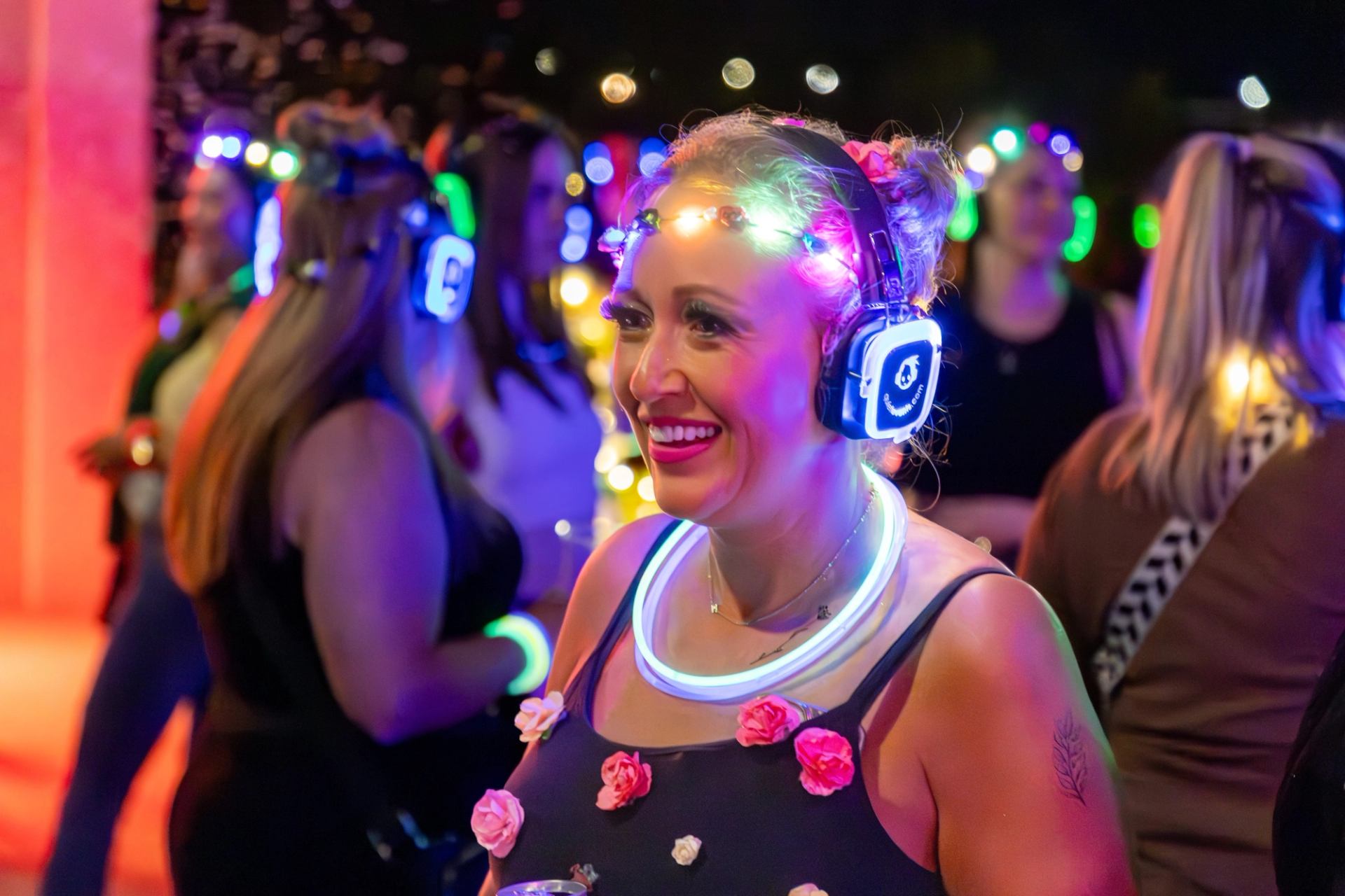 People at a silent disco wearing glowing headphones and neon accessories in dim light.