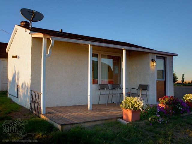 Cozy white cottage with porch seating and flower pots in warm evening light.