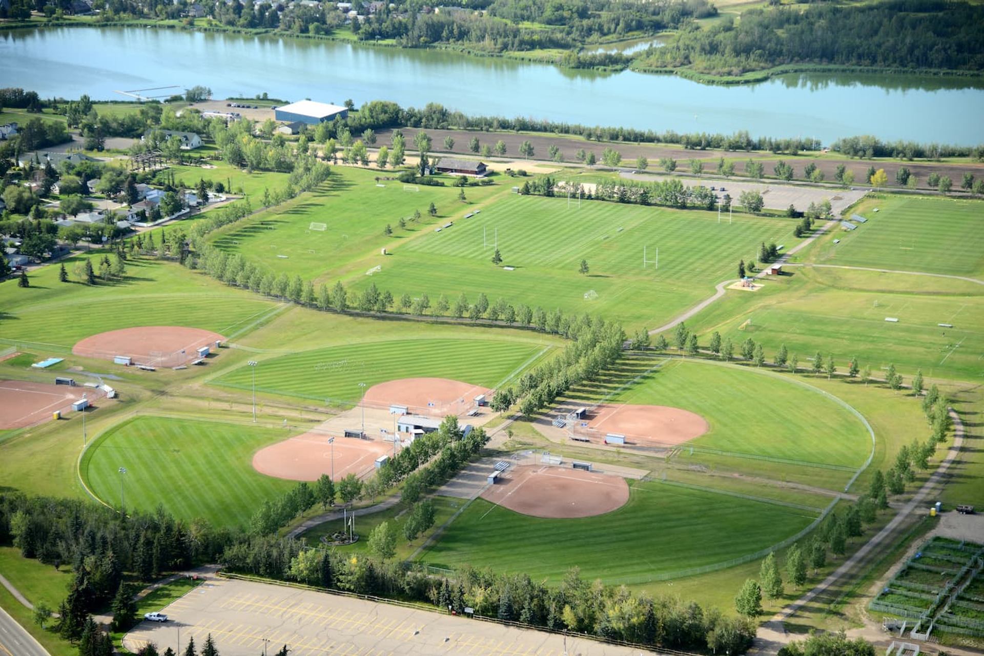 Aerial view of multiple baseball diamonds, soccer fields and trees beside a river.