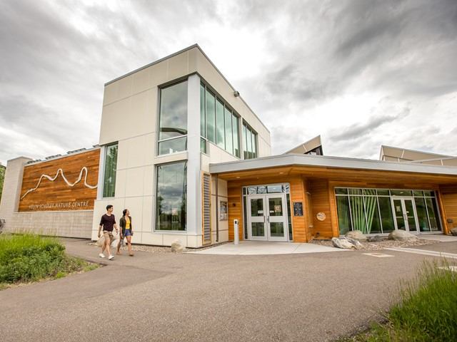 Modern nature centre with glass walls, wood accents, and visitors on pathway.