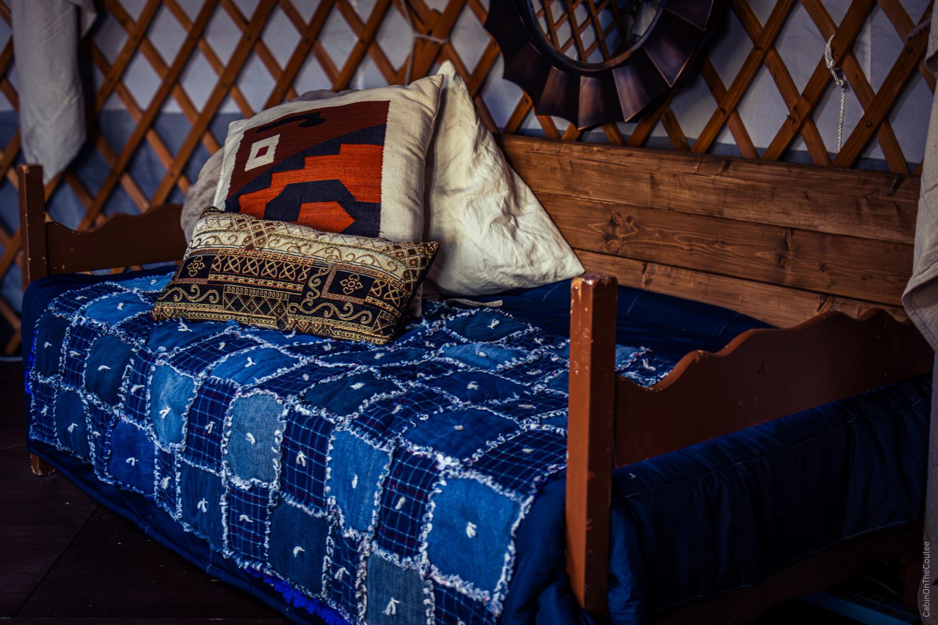 Wooden daybed with patterned pillows and blue quilt inside the yurt.