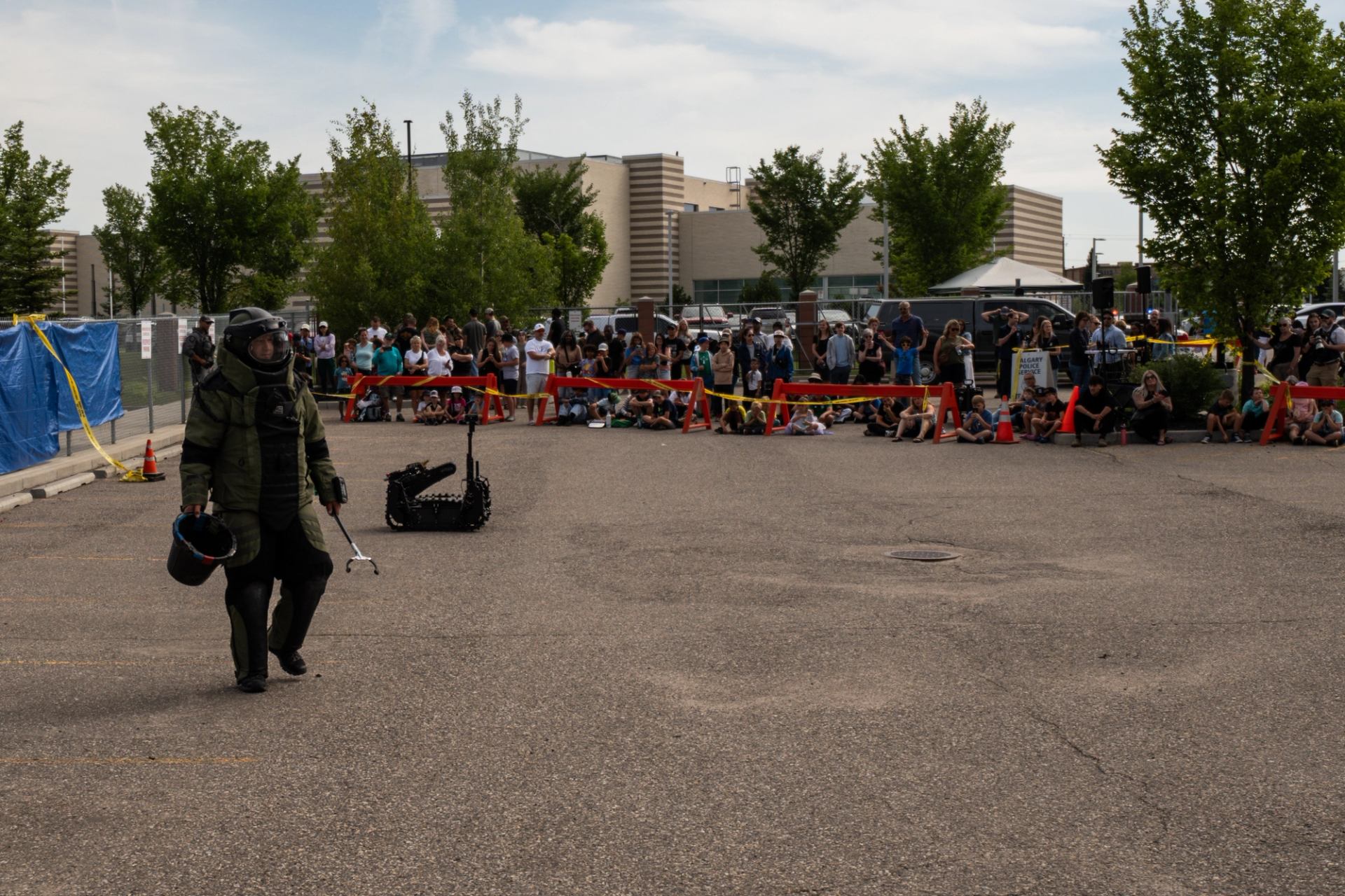 Bomb squad member walks near a robot as spectators watch behind barriers.