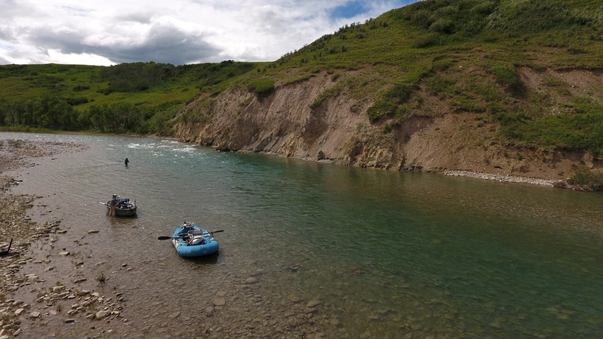 Rafts rest in a clear river beside rocky, green hills.