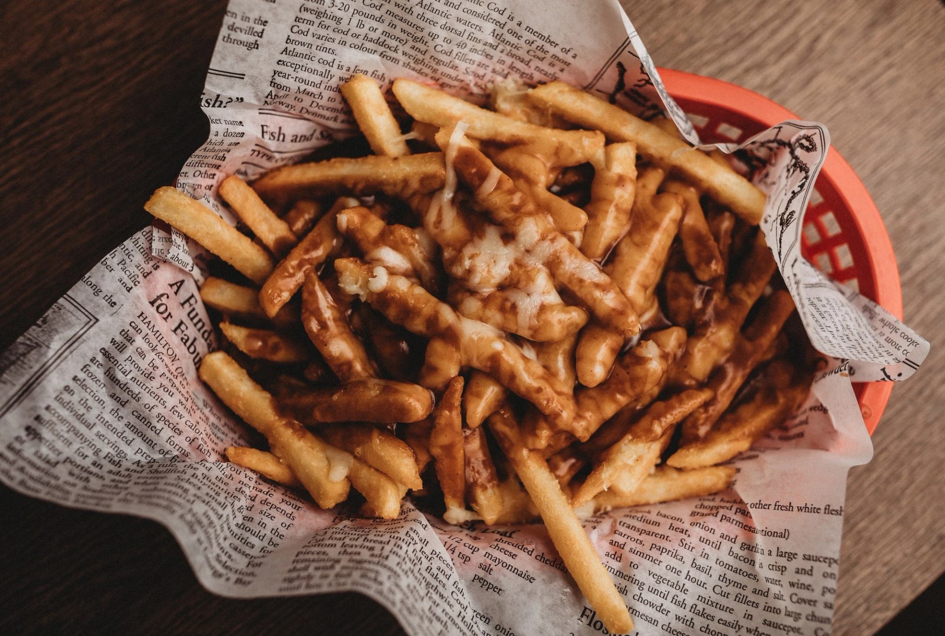 Basket of French fries on newspaper with dipping sauces in a red tray.