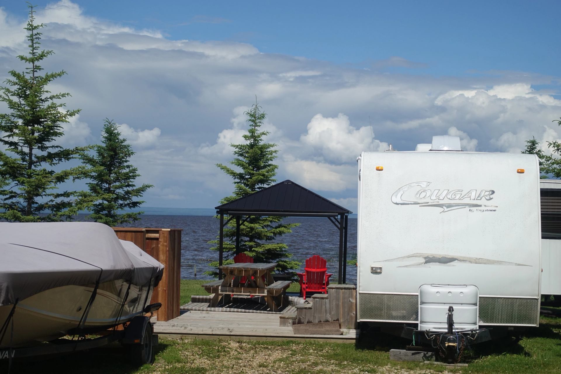 A trailer, sitting area, and boat on a lakeside RV lot.