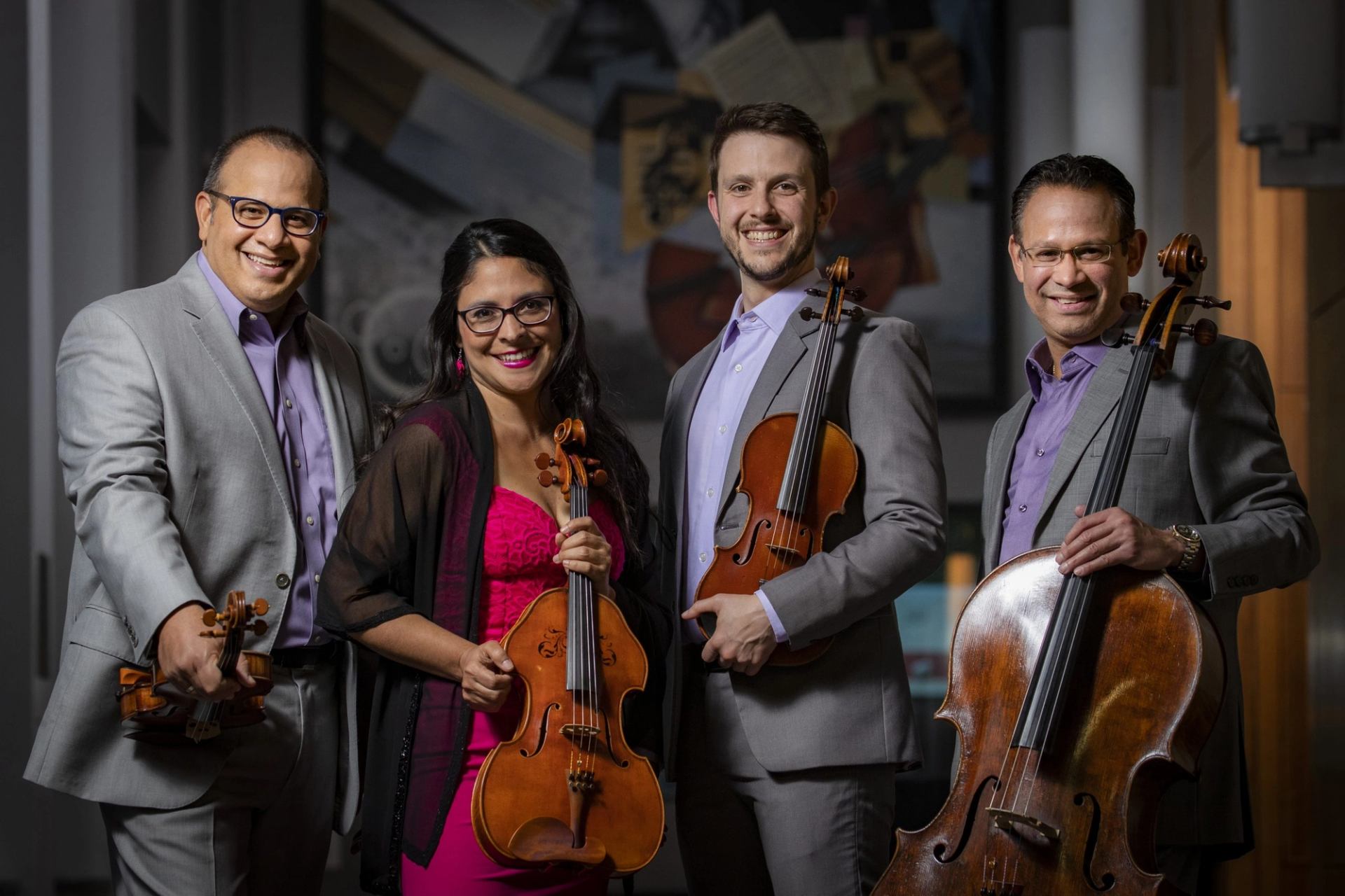 String quartet musicians in suits hold violins, viola and cello in an indoor setting.