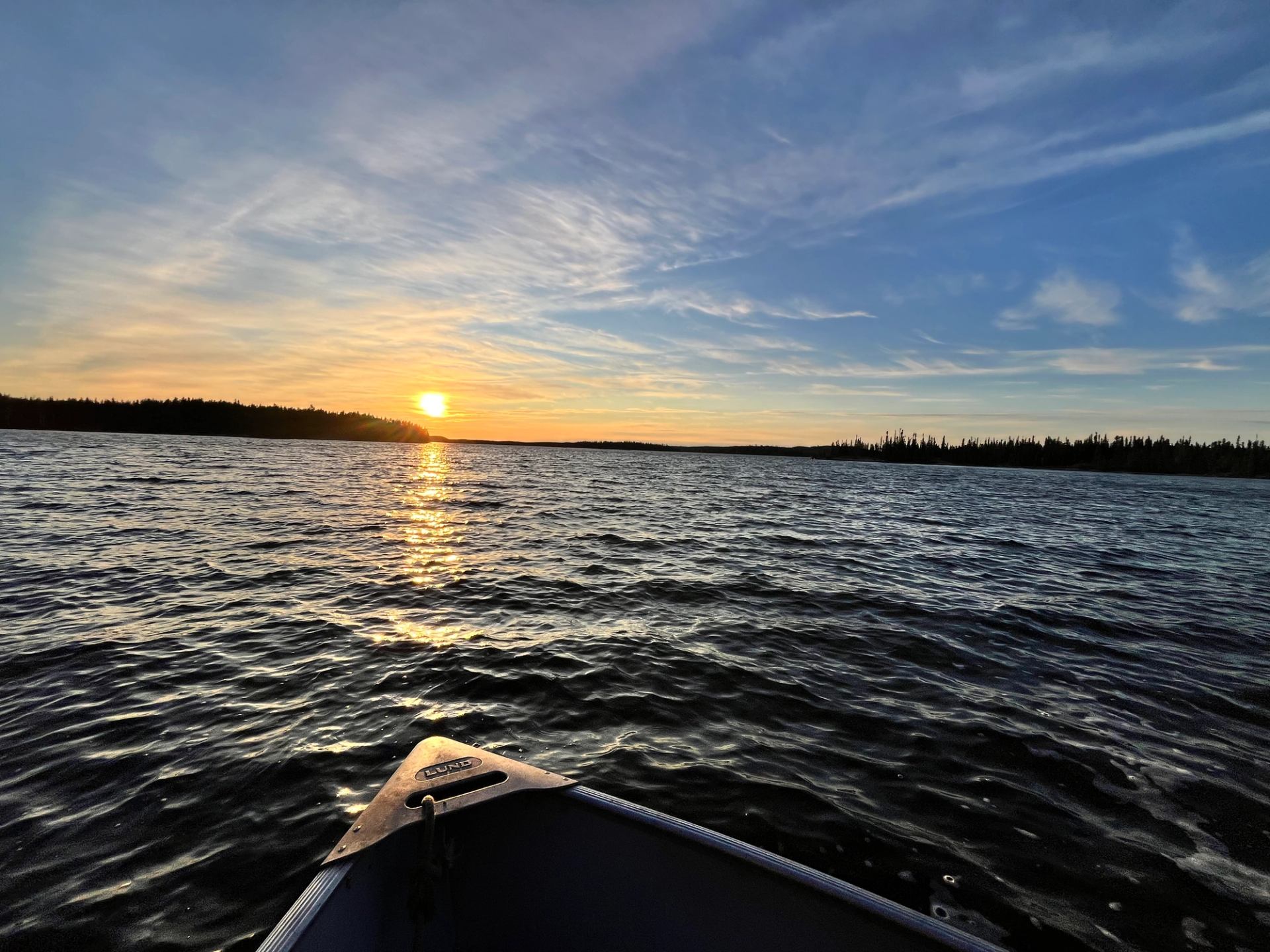 Sunset view from boat with glowing sky and rippling water.