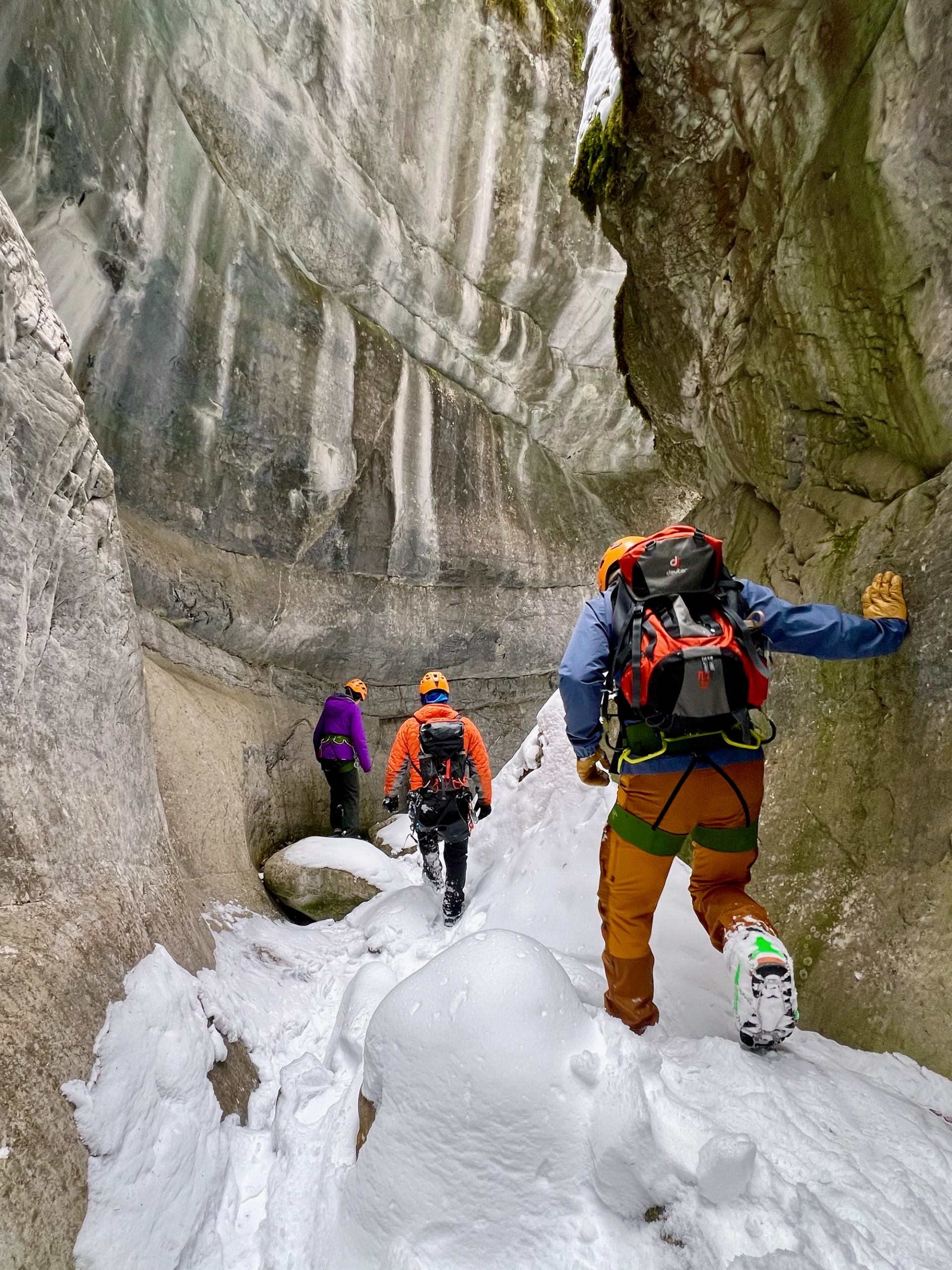 Group walking through a narrow icy canyon with snow-covered ground and tall walls.