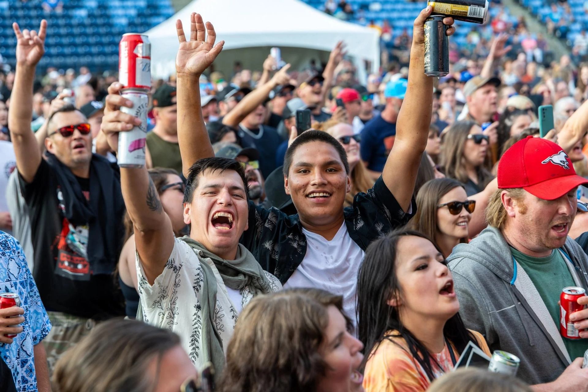 Crowd at outdoor concert with people raising arms and holding drinks near stage.