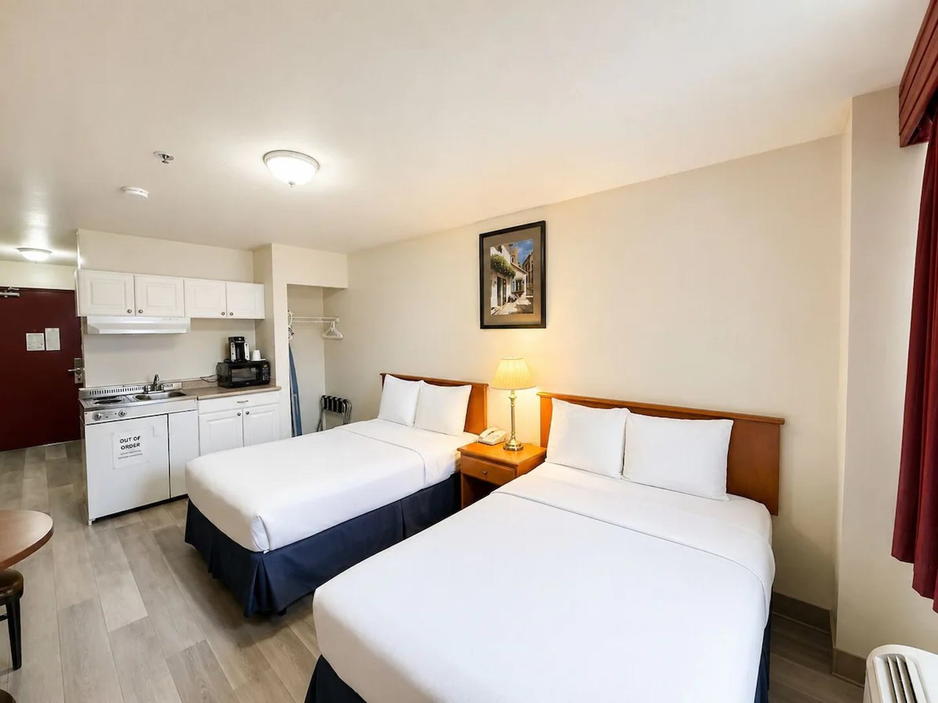 A guest room features two beds, a kitchenette, a microwave, and a bedside lamp.