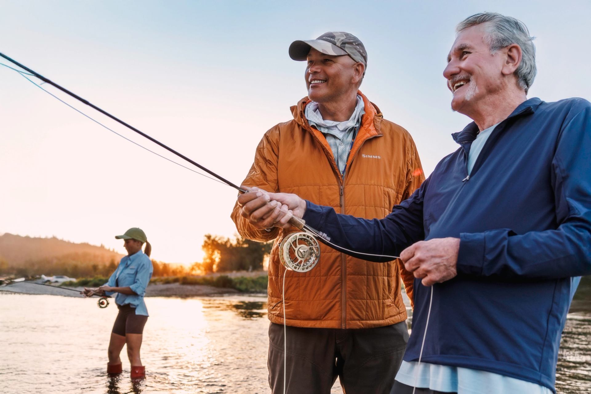 Three people happily fly fishing in a river at sunset.