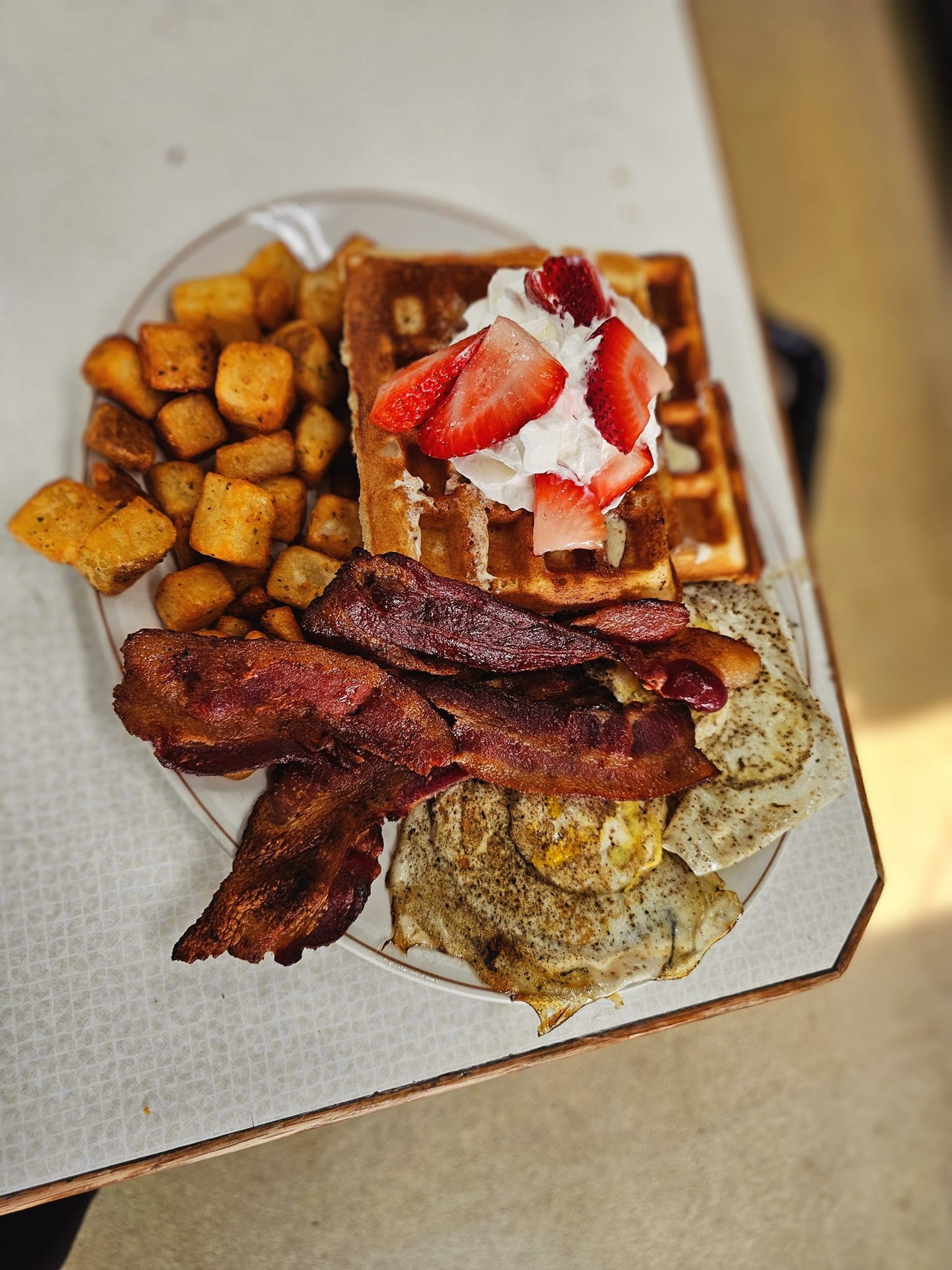Plate with waffles, strawberries, bacon, eggs, and potato tots.