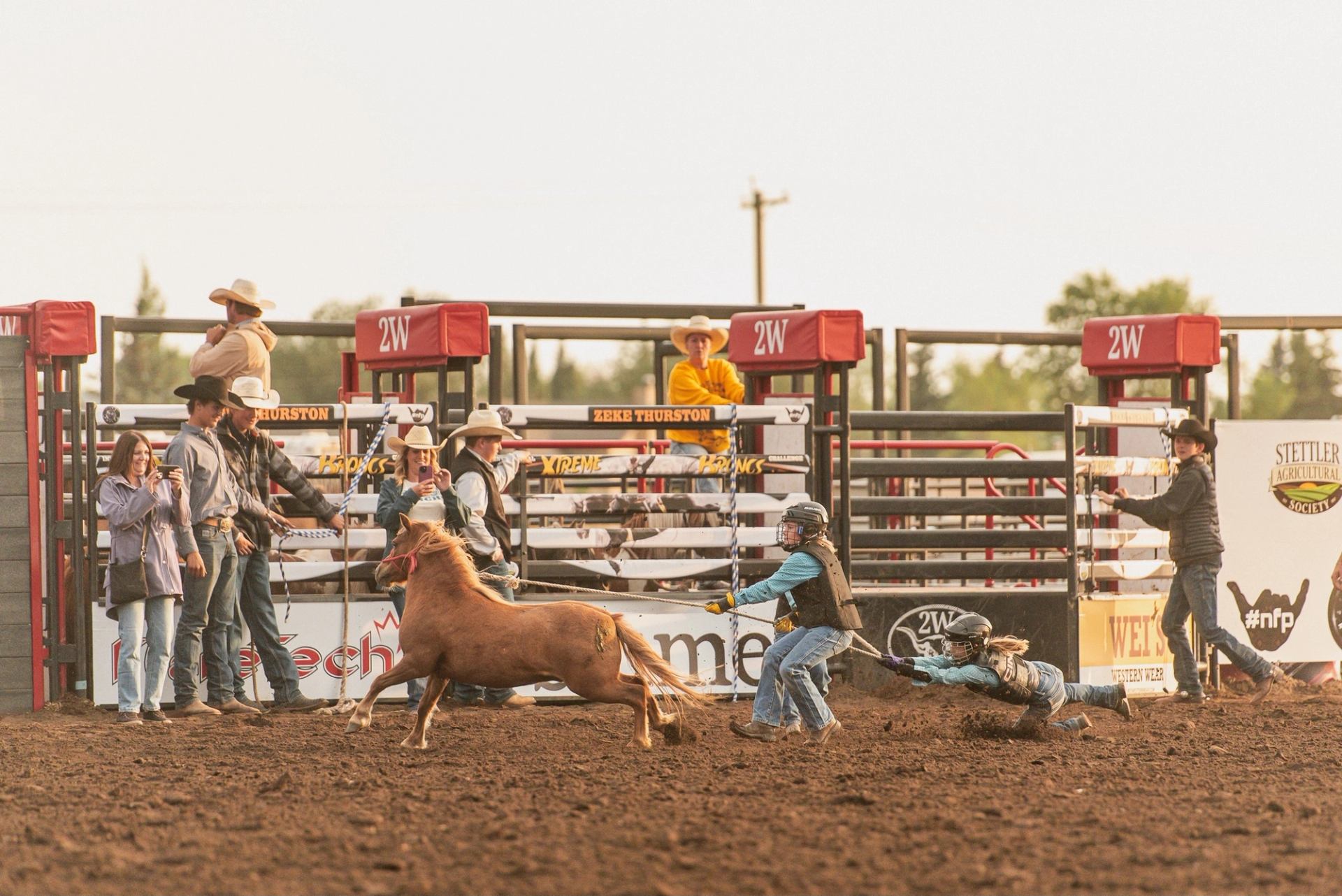 Rodeo arena event with cowboys, bull, and officials in front of chutes.