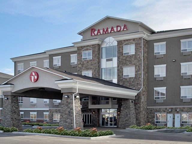 Exterior of Ramada Stettler with stone pillars, red logo, and landscaped entrance.