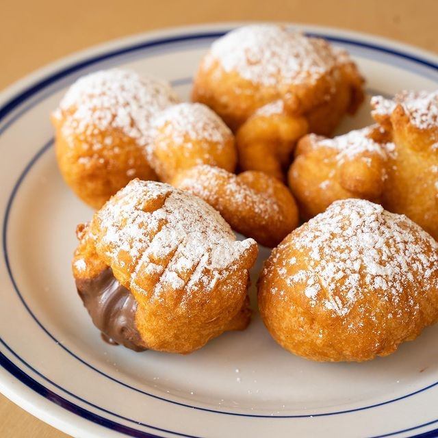 Fried pastries dusted with powdered sugar, one filled with chocolate.