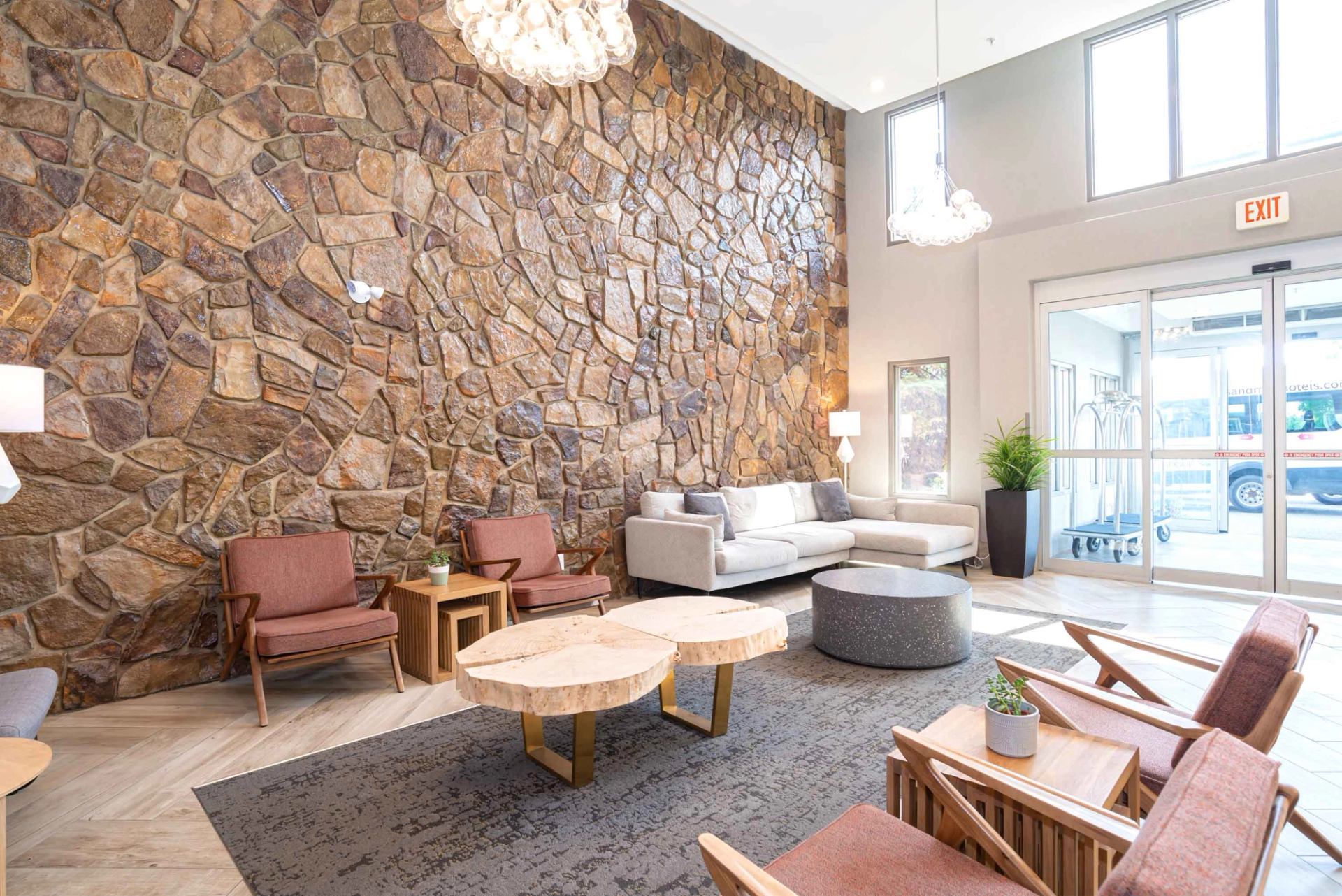 Hotel lobby with stone feature wall, modern seating, coffee tables and glass entrance doors.