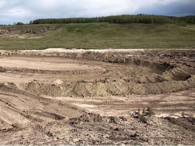 Race track earthworks and dirt track beside grassy hillside under cloudy sky.