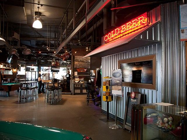 Sports bar interior with neon signs, bar seating, and game tables.