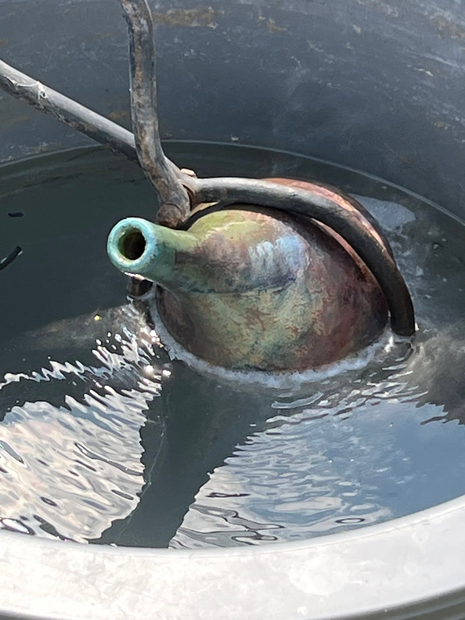 Ceramic teapot-shaped fountain head partially submerged in rippling water inside a basin.