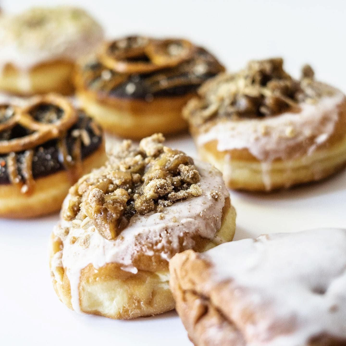Donuts topped with nuts, icing, and pretzels on a white surface