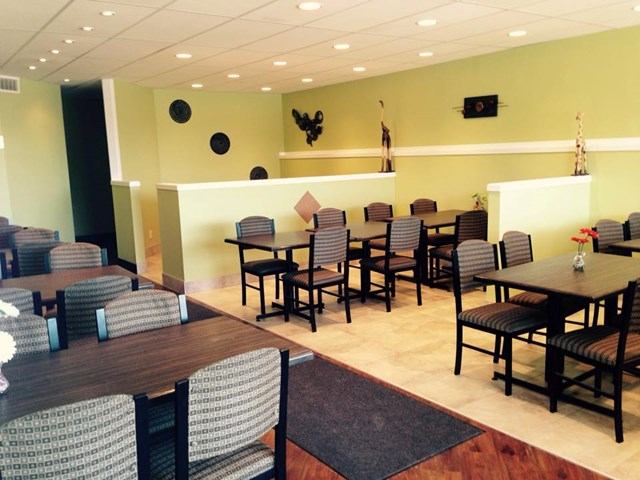 Restaurant dining room with dark tables, patterned chairs, green walls and wall art.