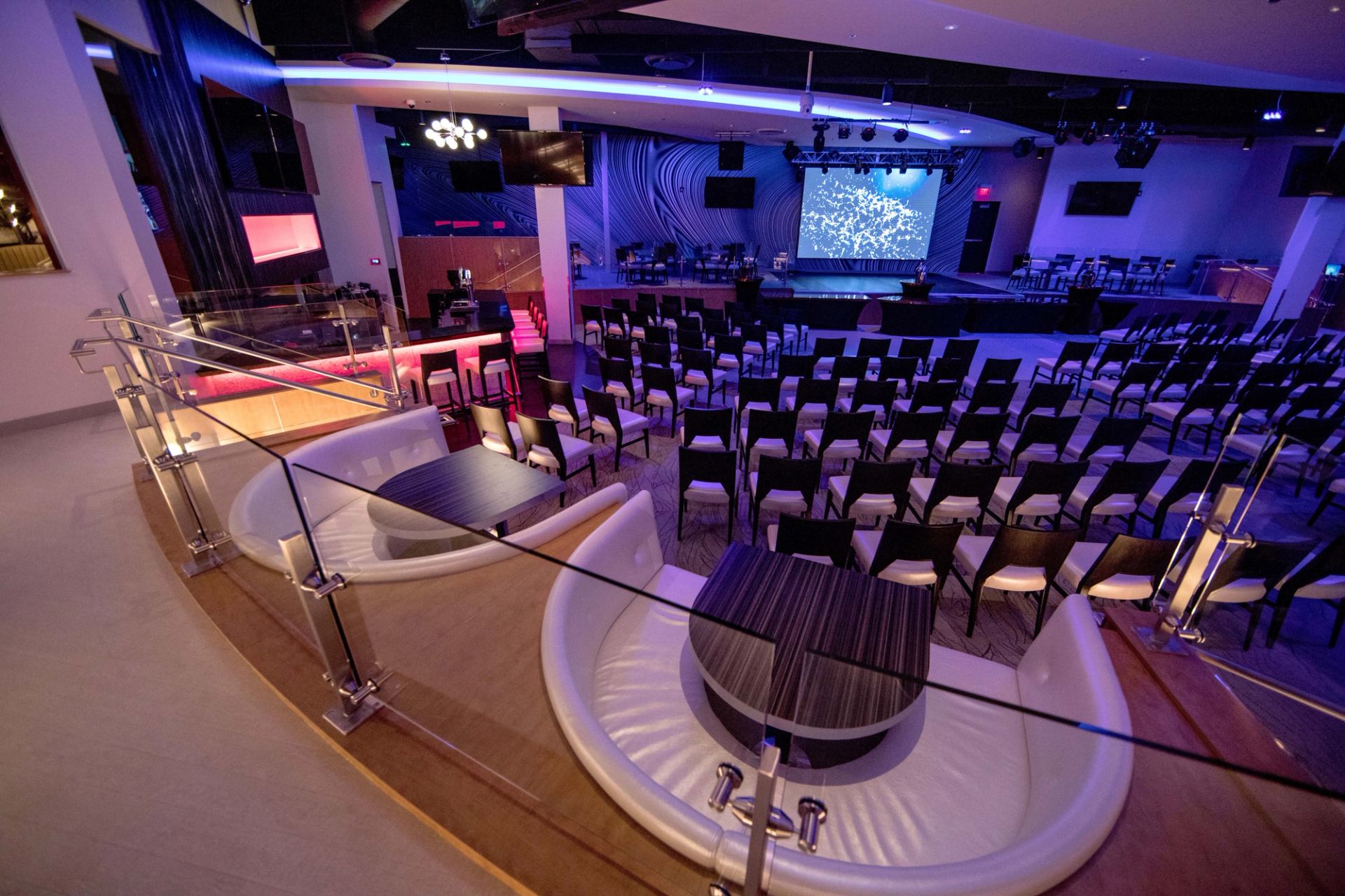 Event hall with rows of chairs facing stage and large projection screen.