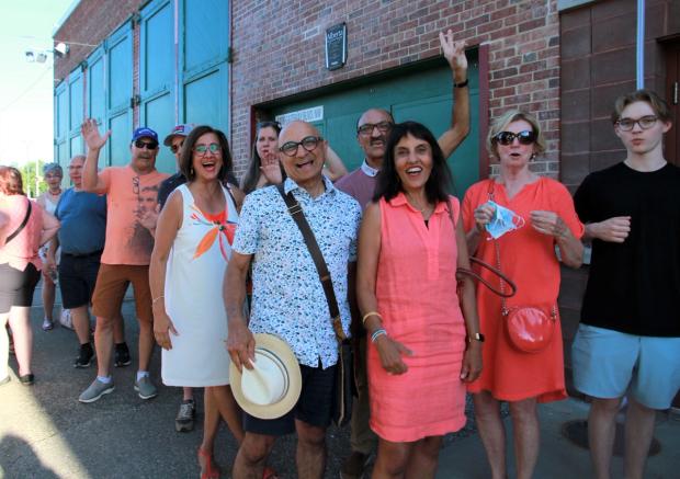 Enthusiastic, smiling people lined up to see a show inside the Arts Barns, grinning and waving at the camera.