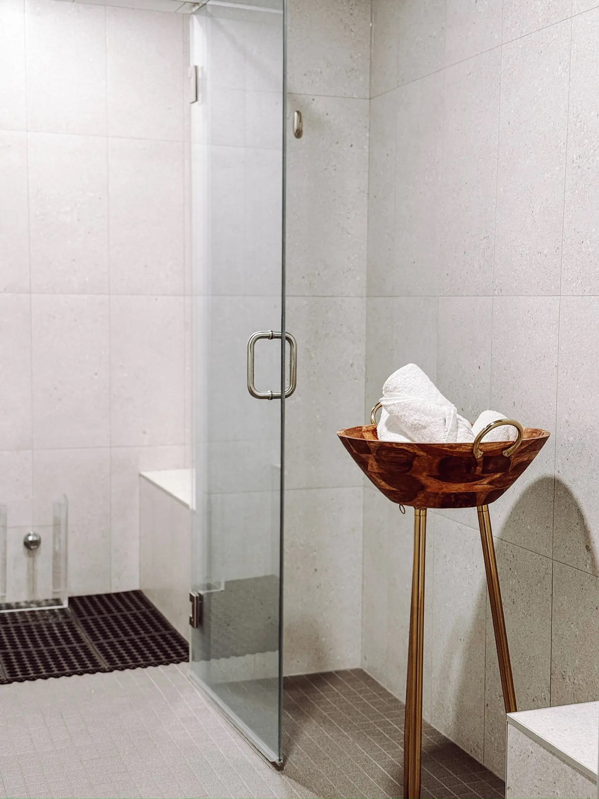 Minimal spa room with a glass shower and a wooden bowl holding towels.