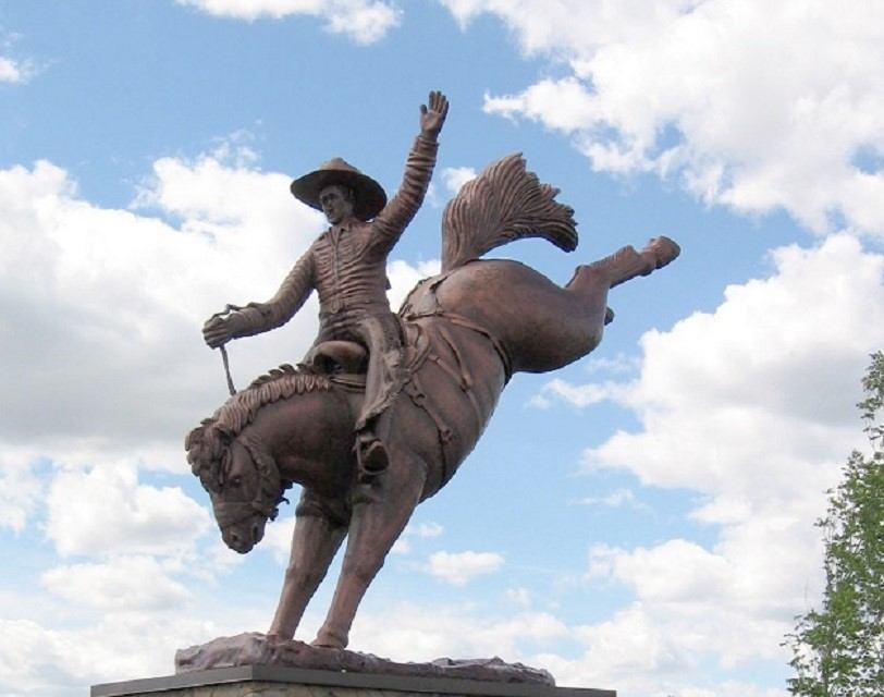Statue of bucking bronc and rider against cloudy sky.